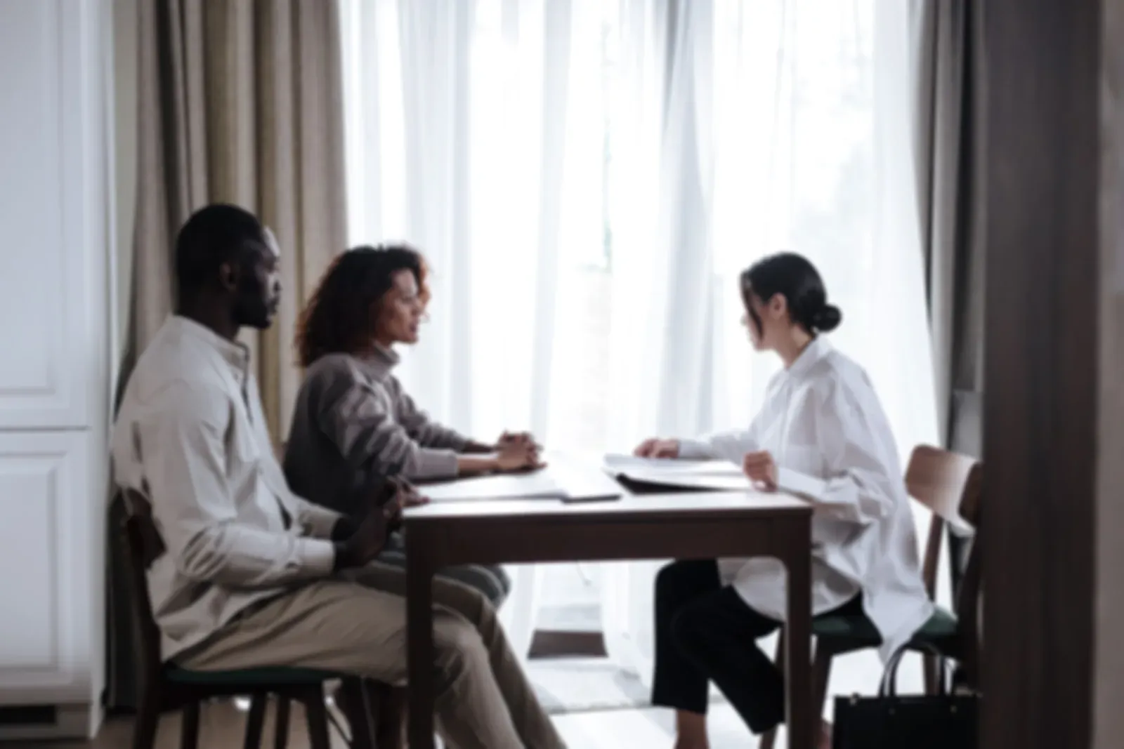 Three people discussing documents at a table by a window